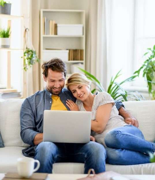 Un couple consulte des annonces immobilières sur un ordinateur portable assis sur un canapé