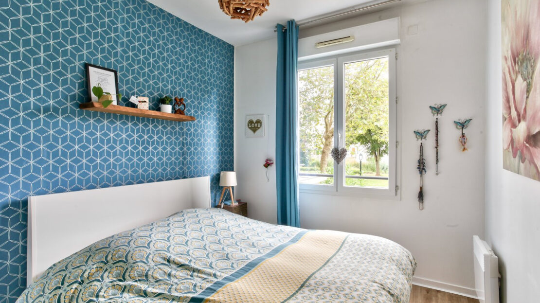 Une chambre bleue avec du parquet, un lit double et vue sur le jardin.