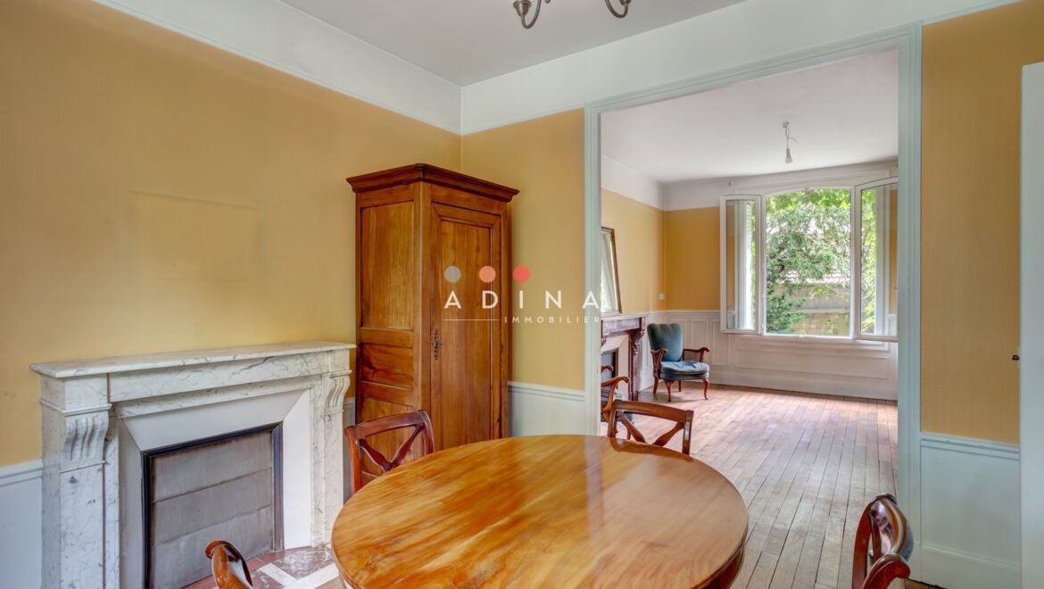 Salle à manger avec cheminée et table en bois, vue sur salon lumineux.