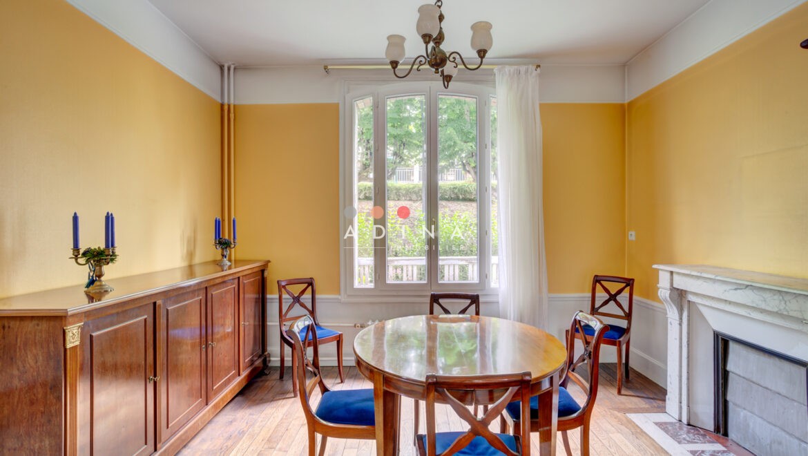 Salle à manger lumineuse avec table en bois, chaises, buffet et cheminée.