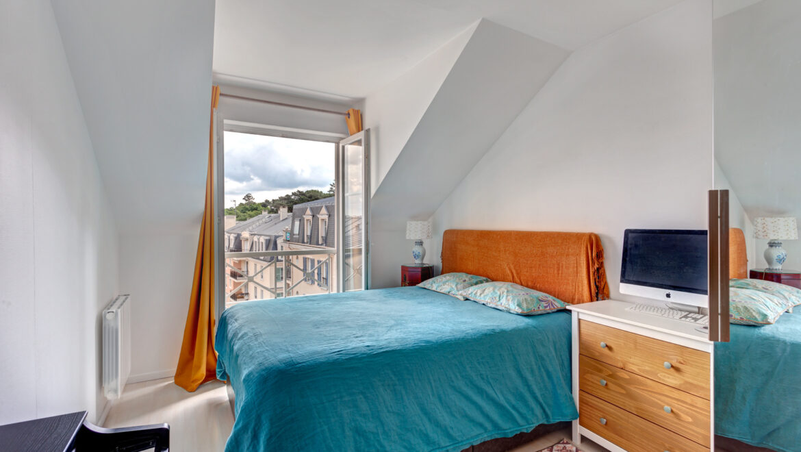Chambre lumineuse avec fenêtre ouverte et toit mansardé.