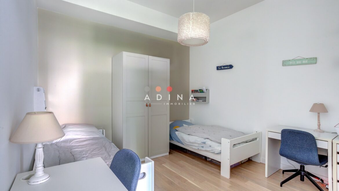 Chambre lumineuse avec deux lits et bureaux.