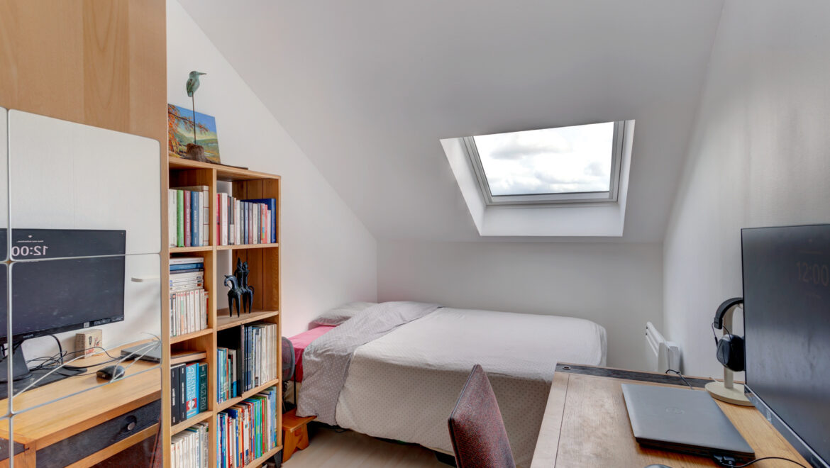 Chambre sous combles avec lit, bureau et bibliothèque.