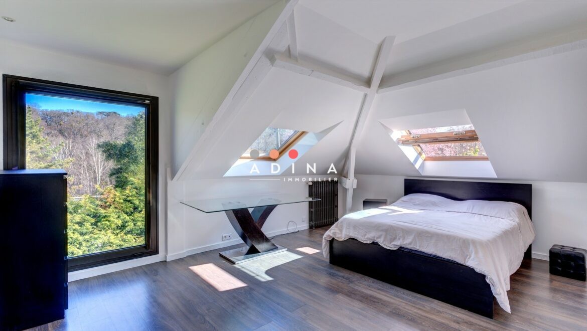 Chambre sous combles avec grandes fenêtres et vue sur la forêt.