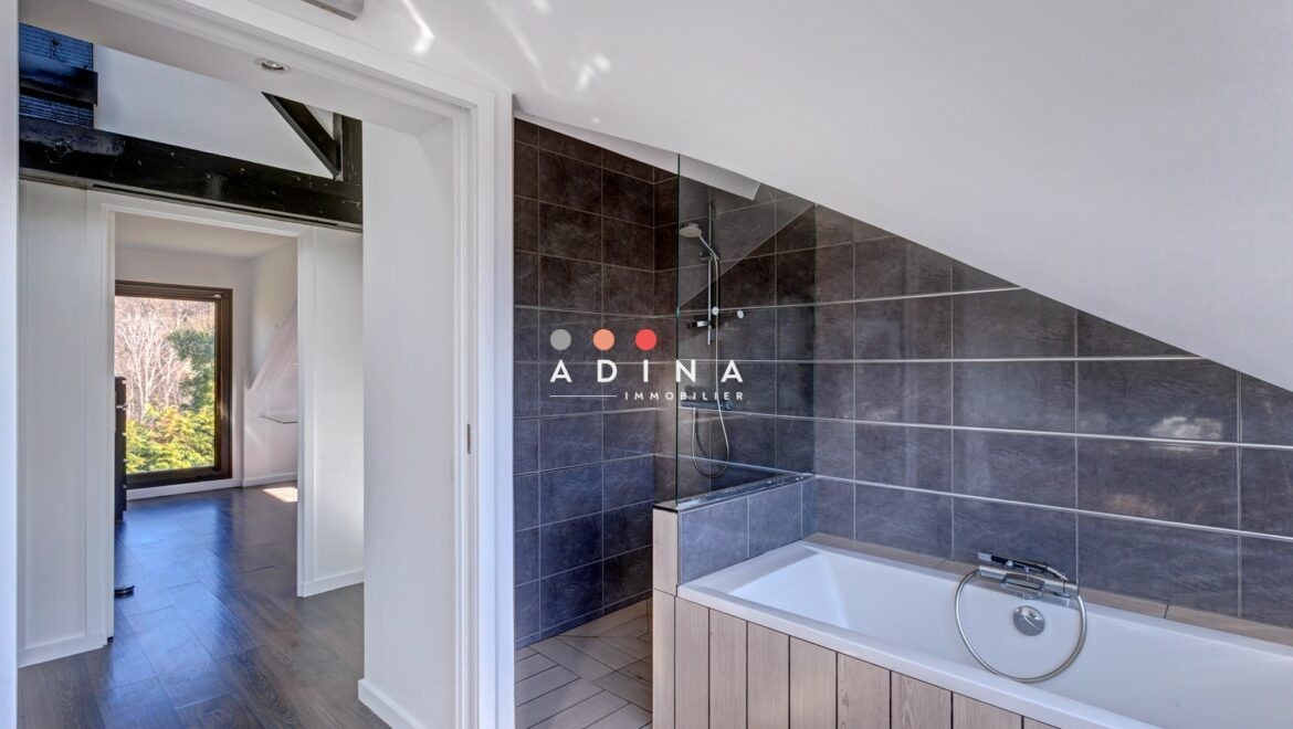 Salle de bain moderne sous mansarde avec baignoire et carrelage foncé.