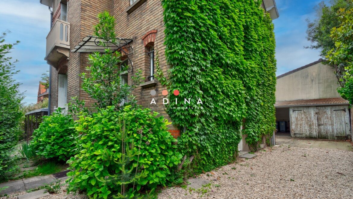 Maison en briques avec vigne vierge et allée gravillonnée.