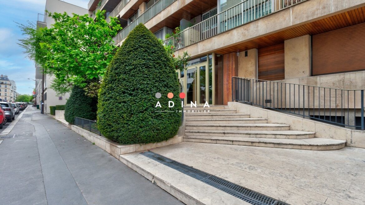 Immeuble moderne à Neuilly-sur-Seine avec entrée en pierre et végétation.