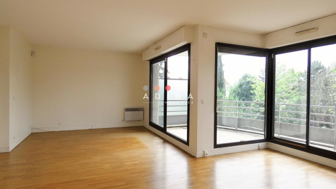 Salon vide avec parquet et grandes baies vitrées.