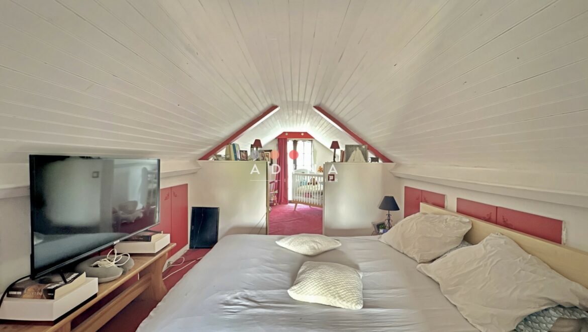 Chambre mansardée avec lit et télévision.