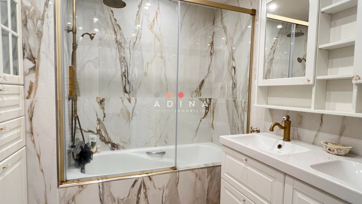 Salle de bain moderne avec carrelage effet marbre et meuble lavabo blanc.