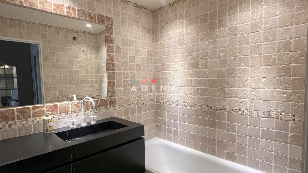 Salle de bain avec baignoire, lavabo noir et carrelage beige.