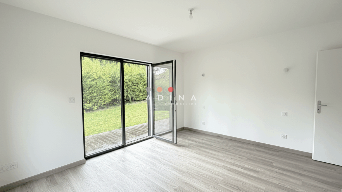 Chambre vide avec parquet, porte-fenêtre ouverte sur jardin.