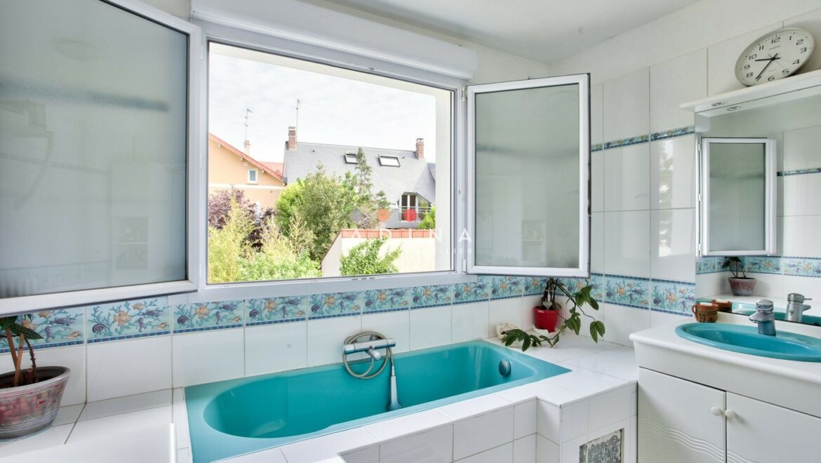 Salle de bain avec baignoire turquoise et vue sur jardin.