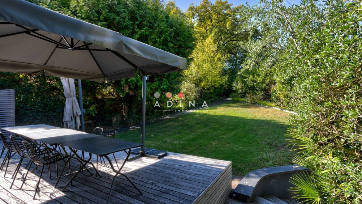 Terrasse en bois avec parasol et vue sur jardin verdoyant.
