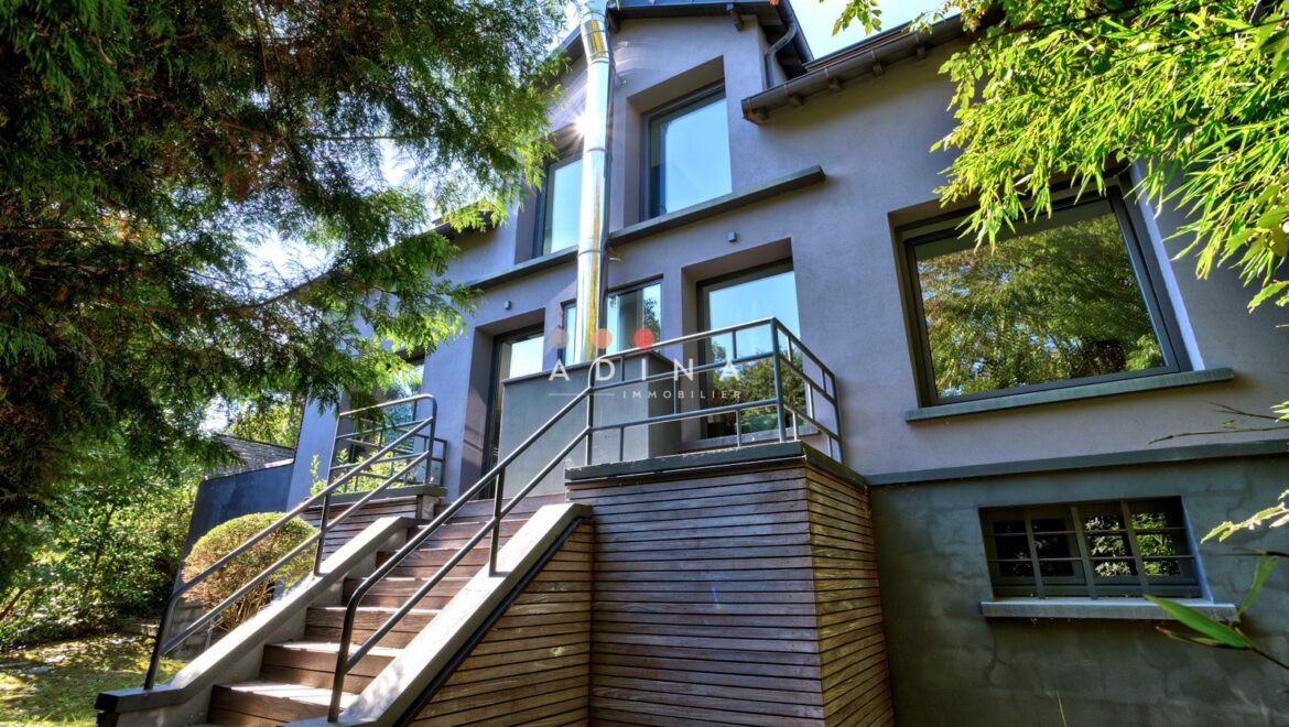 Maison moderne avec escalier en bois et grandes fenêtres.