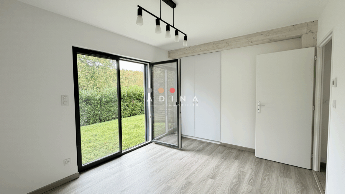 Chambre vide avec porte-fenêtre donnant sur un jardin.