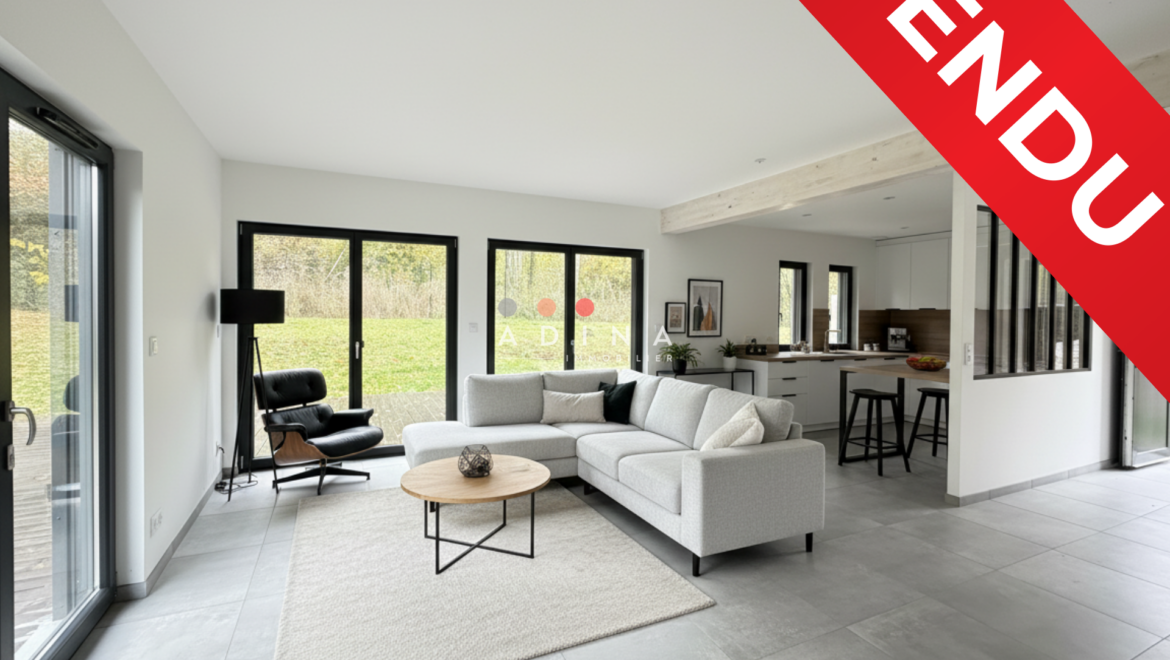 Salon moderne avec canapé beige et panneau "Vendu".