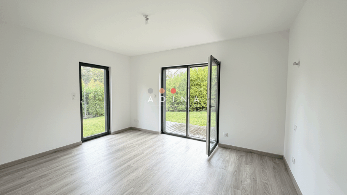 Salle vide avec parquet et baie vitrée donnant sur jardin.