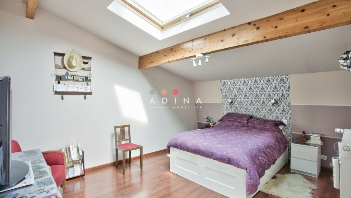 Chambre sous combles avec puits de lumière et poutres apparentes.
