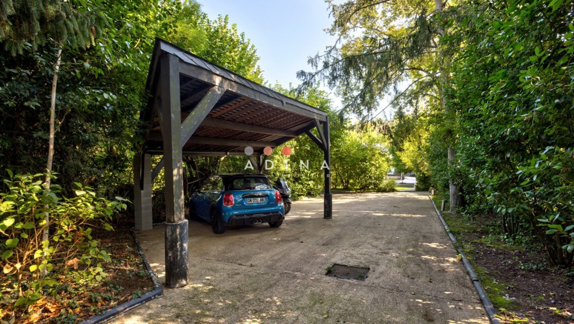 Carport avec voiture bleue et végétation environnante.