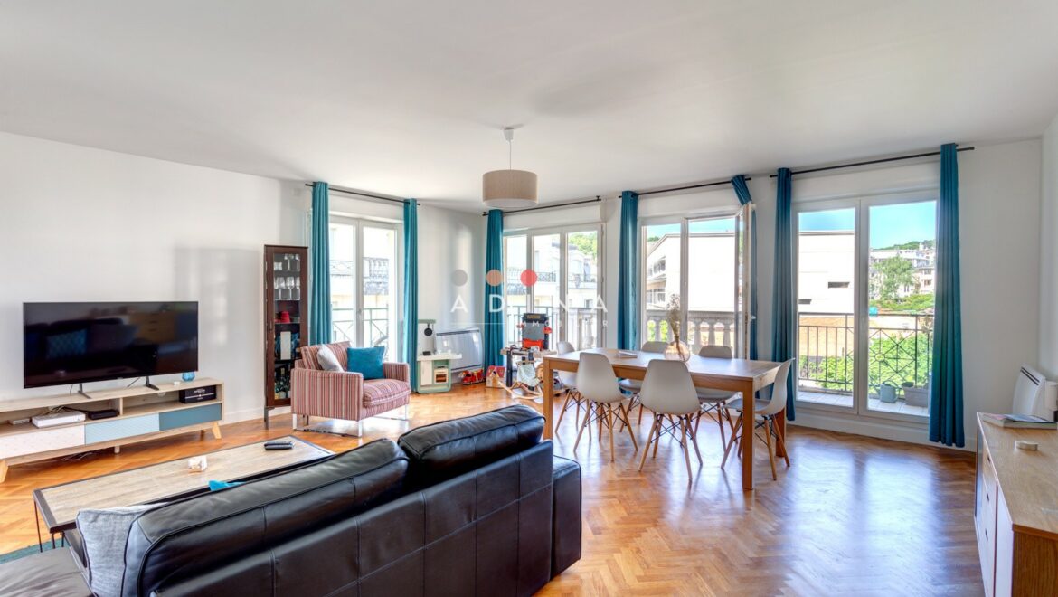 Salon lumineux avec parquet et grandes fenêtres.