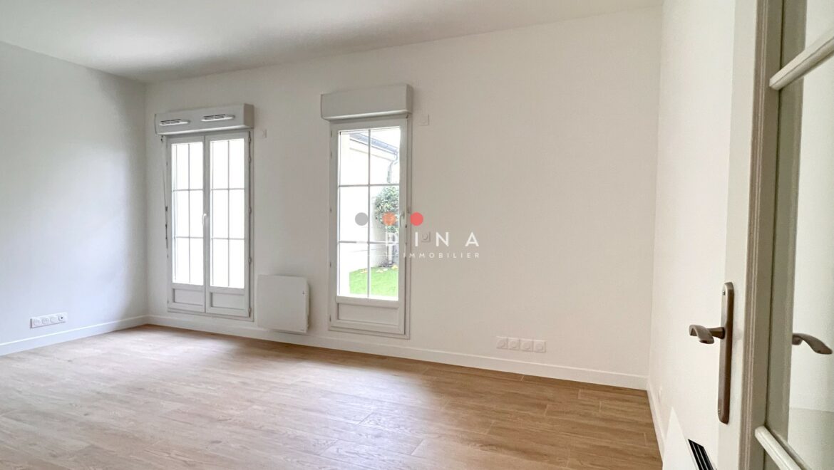 Salle de séjour vide avec parquet et grandes fenêtres.