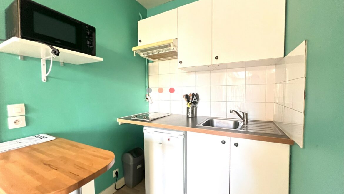 Cuisine compacte avec mobilier blanc et mur turquoise.