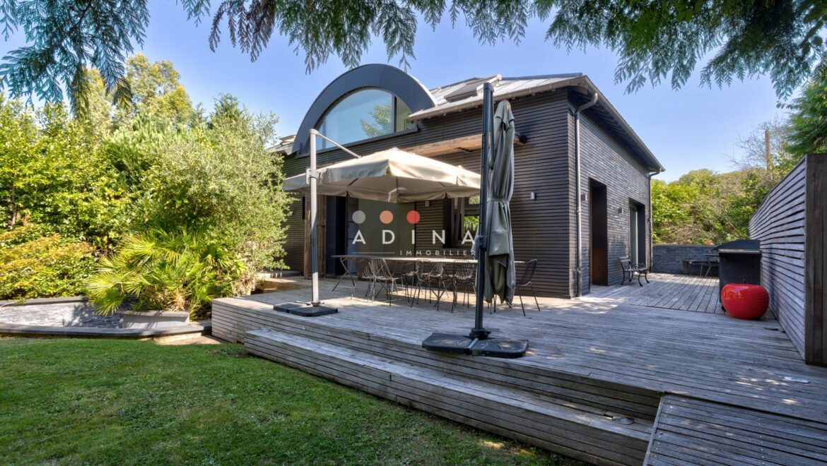 Maison moderne avec terrasse en bois et jardin verdoyant.