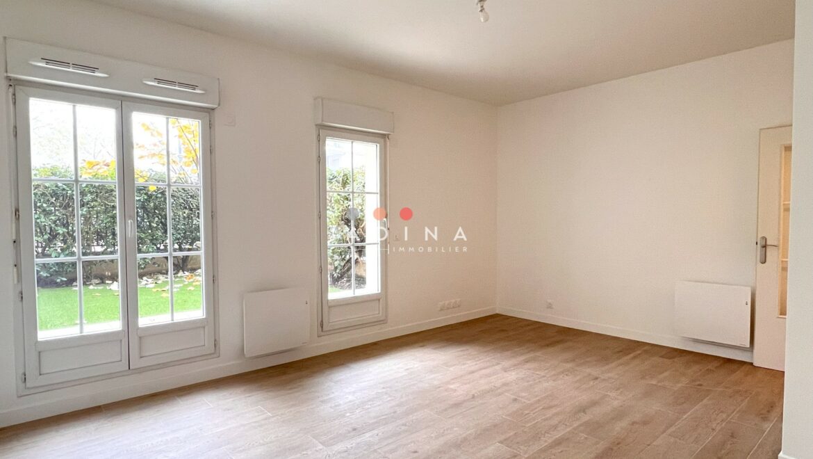 Salle de séjour lumineuse avec parquet et grandes fenêtres.