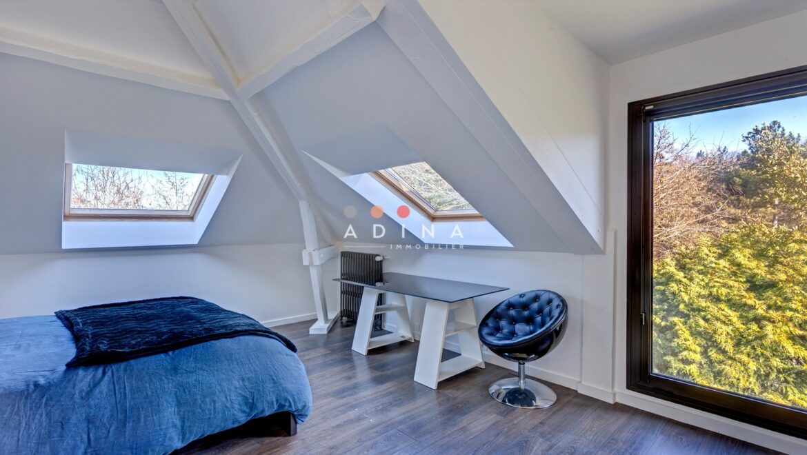 Chambre mansardée avec fenêtres de toit et vue sur la forêt.