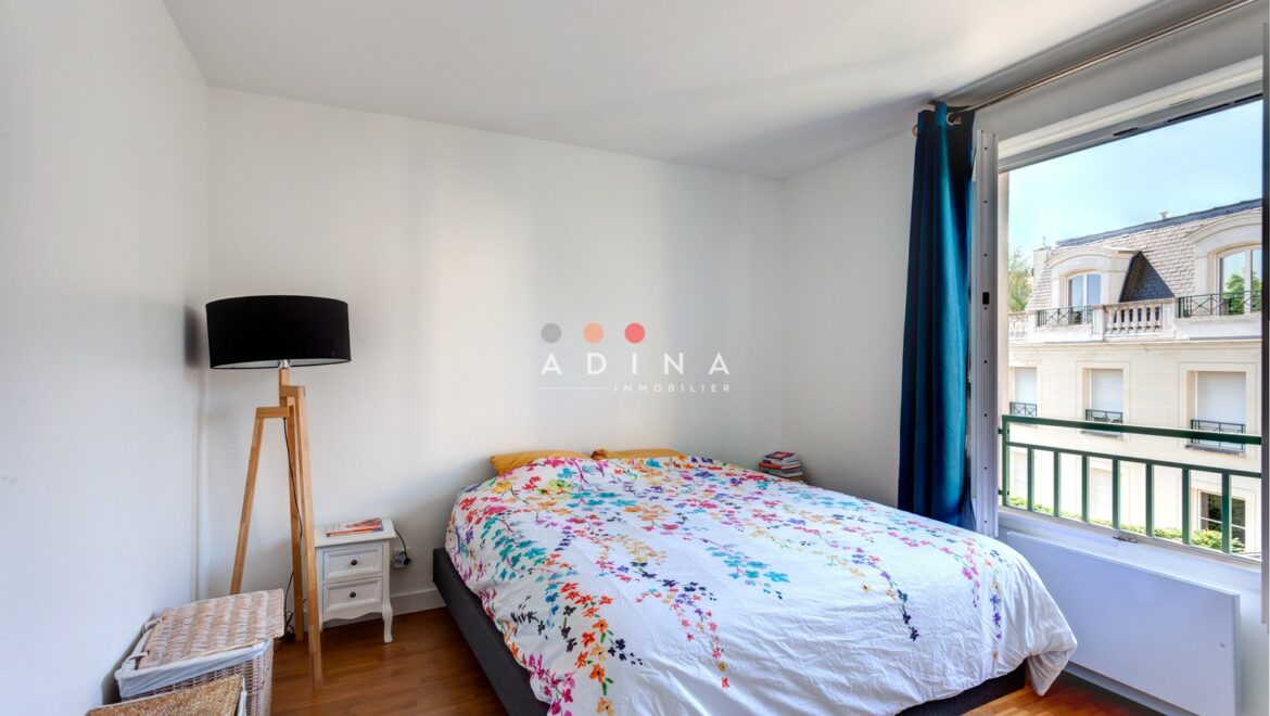 Chambre lumineuse avec lit à motifs floraux et fenêtre ouverte.