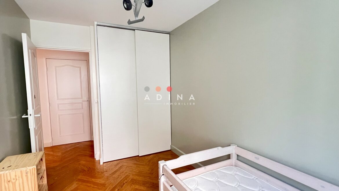 Salle avec lit d'enfant, parquet bois, et armoire blanche.