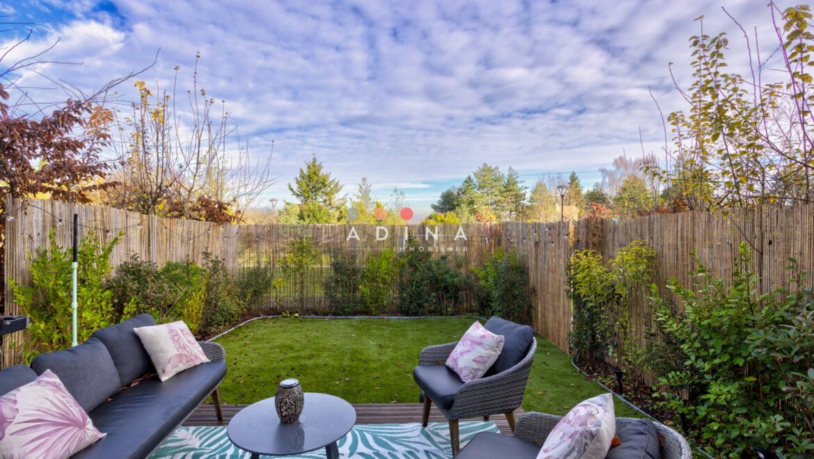 Jardin avec terrasse aménagée et ciel nuageux.