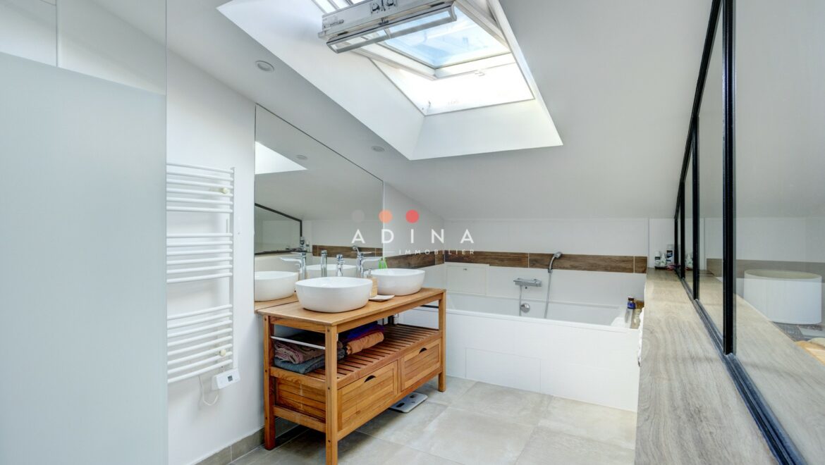 Salle de bain moderne sous les combles avec baignoire et double vasque.