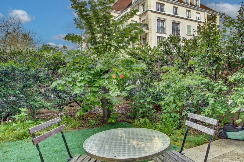 Terrasse d'un jardin avec table et chaises, bâtiment en arrière-plan.