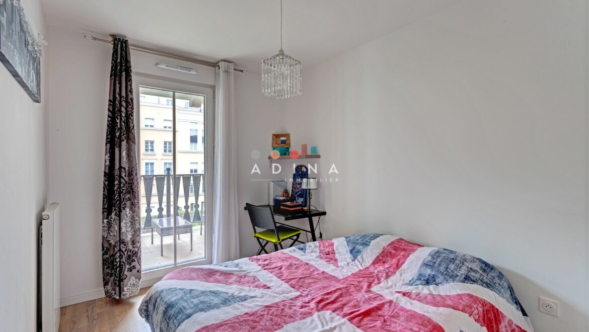 Chambre lumineuse avec lit et petit bureau près d'une fenêtre.