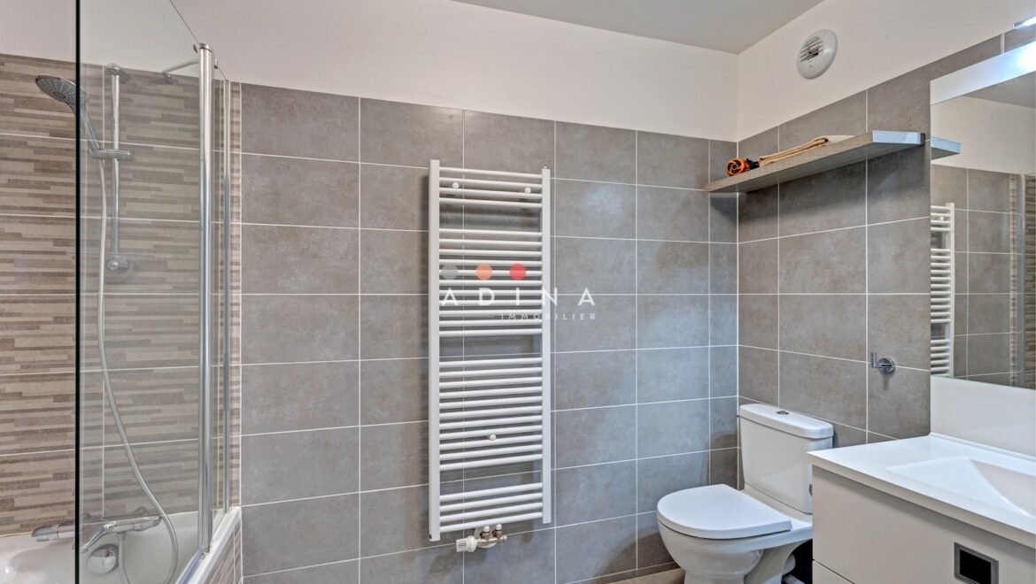 Salle de bain moderne avec douche et carrelage gris.