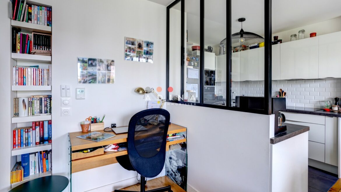 Coin bureau avec verrière intérieure donnant sur une cuisine moderne.