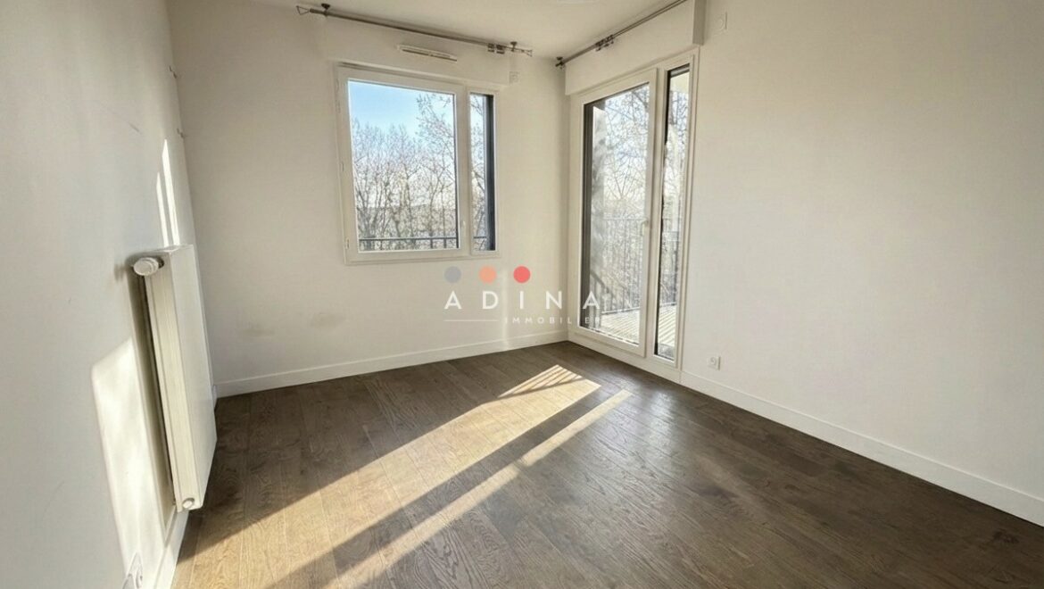 Chambre vide avec parquet et grandes fenêtres.