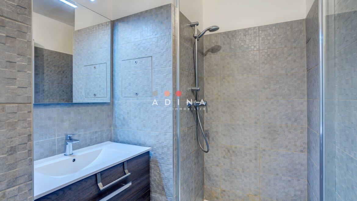 Douche moderne avec carrelage gris et lavabo.